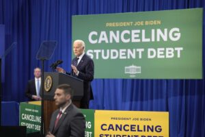 President Biden stands at a podium with a large green banner reading "Cancelling Student Debt" behind him.
