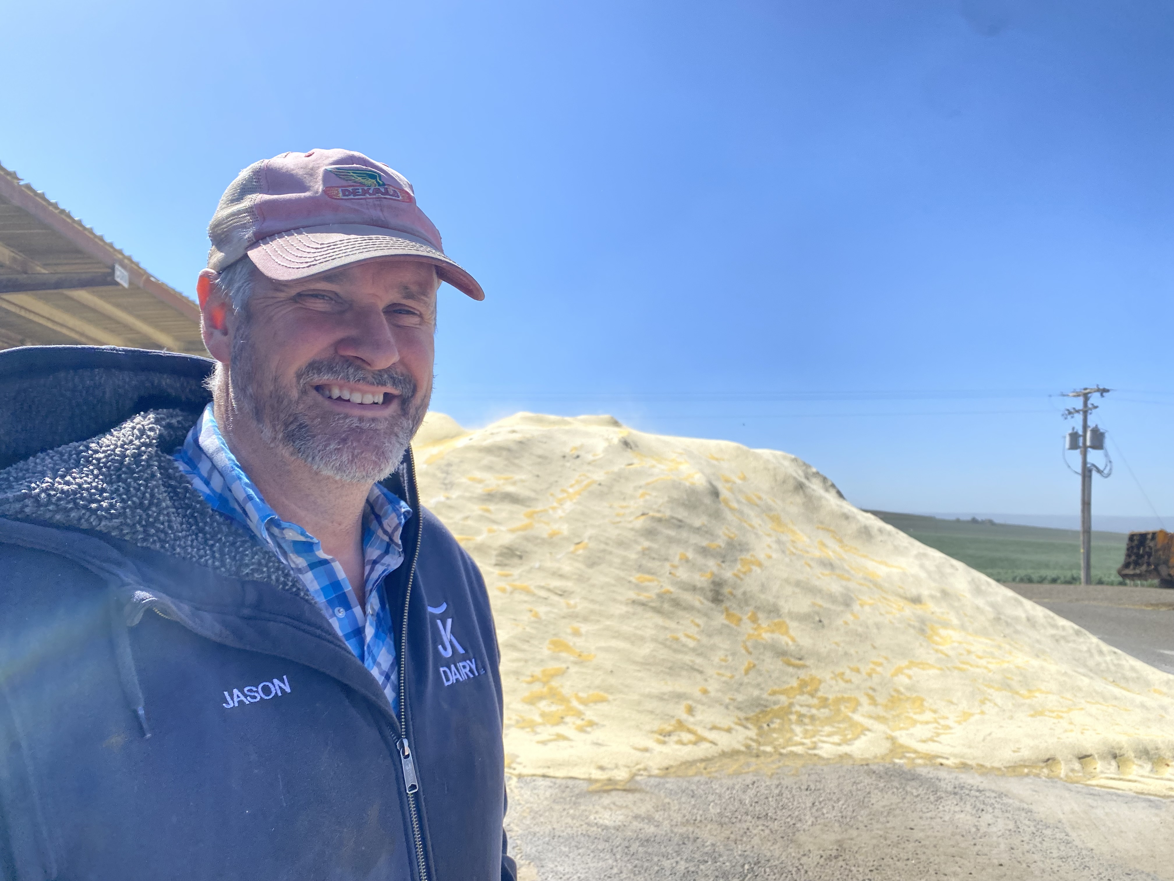 Jason Sheehan grins April 19, despite the tough conditions and water situation this year, in front of a pile of corn for his cattle, four miles east of Sunnyside, Washington.